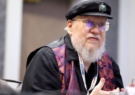 george-r-r-martin-sitting-at-a-convention-in-front-of-a-mic.jpg